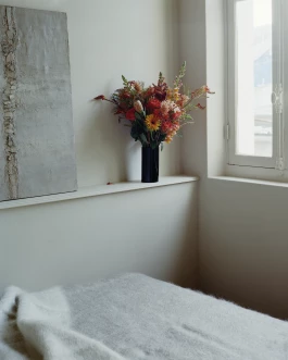 beige-grey painted bedroom featuring mohair blanket by Brun de Vian Tiran, colourful floral arrangement and art piece 
