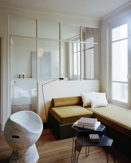 living room with large partitioned glass verrière, green gold velvet sofa, wool bouclé cushions, matégot style coffee tables, Willy Guhl fibre cement chair 