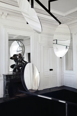 three round mirrors attached to oblique, steel structure within an all-white Parisian apartment featuring classical stone sculpture upon a marble mantlepiece 