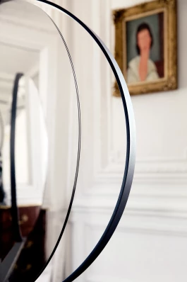 round mirror and detached rounded black steel profile with blurred portrait painted by Modigliani in the background 