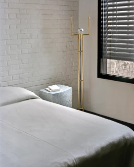 soft light falls on a linen covered bed with a Martin Goerg ceramic bedside table and a designer gold-plated floor lamp by Thomas Duriez 