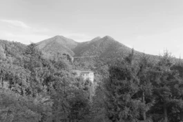 an historic villa sits alone on a ridge with mountains behind 