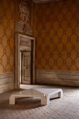Two triangular tables with a crackled ceramic glaze finish in off-white and beige colours, standing side by side in an Italian palace. 