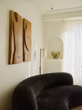 Softly lit living room featuring a voluptuous black velvet sofa and wall-hung carved wooden sculptures. 