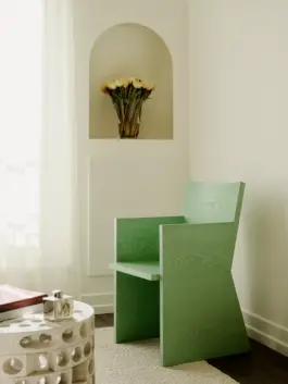A vibrant mint green armchair sits in a warm living room in front of large bouquet of white tulips. 