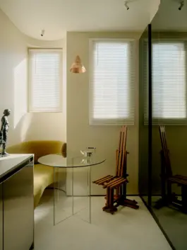 A transparent glass table sits in a dining area with a wrap around upholstered bench in front of smoky mirrored cabinets. 