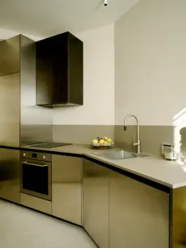 A bowl of lemons on top of brass and aluminium kitchen cabinets that faintly reflect a hazy background. 