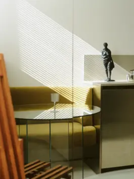 Blinds cast a striking light into kitchen onto a small bronze sculpture of a human figure on top of kitchen workbench. 
