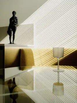 An art deco wine glass with vertical and horizontal stripes in dialogue with shadows cast into kitchen space by blinds and reflected on a glass tabletop. 