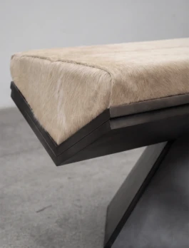 Detail of the Rhomy bench, showing the cowhide cushion and the stepped metallic frame cantilevering over the angled base