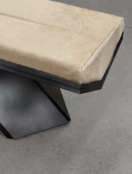 Top-down detail of the Rhomy bench, with its seamed cowhide cushion, faceted frame edge and angled metallic base on a concrete floor